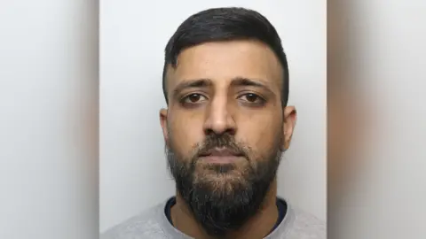 West Yorkshire Police A mugshot of Shamrez Razaq who has black hair combed to one side and a medium length beard. He is wearing a grey jumper.