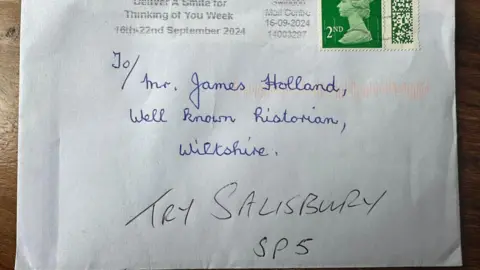 James Holland A white envelope with a second-class stamp addressed, handwritten in blue ink, to Mr James Holland, well-known historian, Wiltshire, with the words try Salisbury SP5 added in black ink underneath.