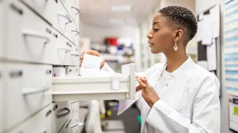 Getty Images A pharmacist opens a draw to get some prescription medication for a patient