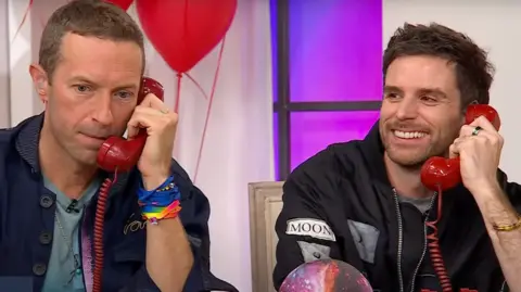 QVC Chris Martin and Guy Berryman of Coldplay take phone calls from fans during an appearance on the shopping channel QVC