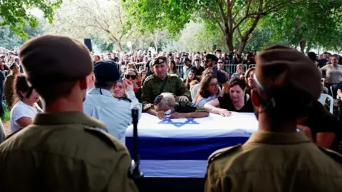 Reuters Large crowds gathered at funeral of Israeli soldier Sergeant Amitai Alon. Family members lean on his coffin crying with Israeli soldiers standing guard in front of it.