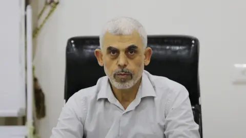 Getty Images A headshot of Yahya Sinwar, wearing a white dress shirt, sitting in a black leather desk chair and staring into the camera