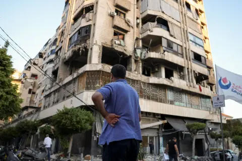 Reuters A Beirut resident stands in front of a building damaged in an Israeli air strike last week.