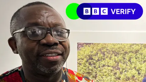 Jonathan Griffin / BBC A head and shoulders portrait of Dr Leo Igwe as he looks at the camera wearing a colourful shirt, with the corner of a photo hung on a wall behind him just visible, showing shrubbery. 