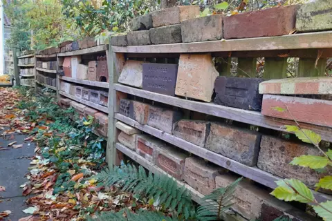 Ian Suddaby Shelves of bricks in various shades of red and brown, in garden. 