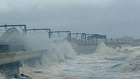 Lawrence/BBC Weather Watchers Waves crash up the sea wall, sending spray over the railway line at Saltcoats in Ayrshire