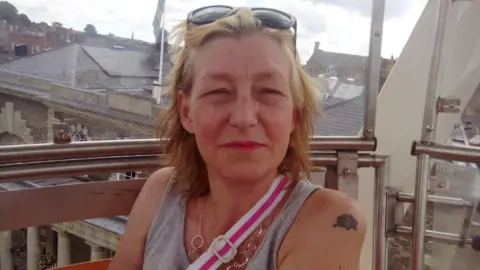 Facebook 44-year-old Dawn Sturgess is pictured smiling on a balcony wearing a grey vest, crossbody bag and sunglasses on her head.