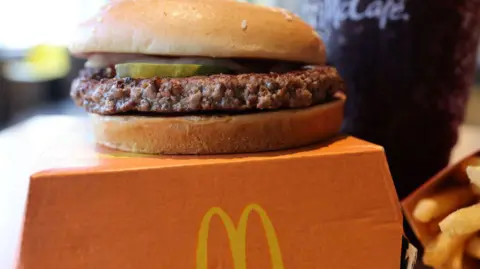 Getty Images A McDonald's quarter pounder sits on an orange takeaway box with a bit of pickle and onion peeking out from under the bun