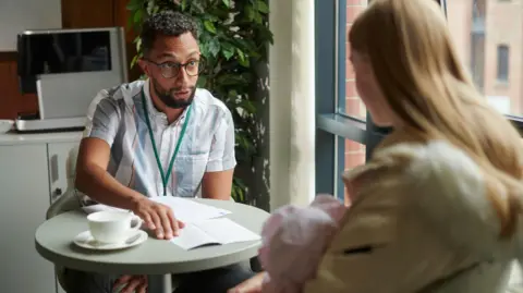 Getty Images Young mother holds a baby while being shown paperwork by a man who appears to be an adviser