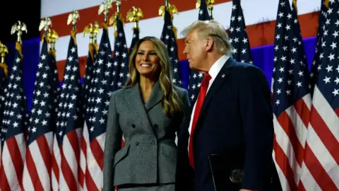 Getty Images Melania Trump and Donald Trump in West Palm Beach, Florida on the early morning of Nov 6, standing on stage before a row of American flags 