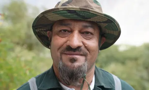 A close up headshot of Ijaz wearing a camo sun hat and who has a goatee-style beard