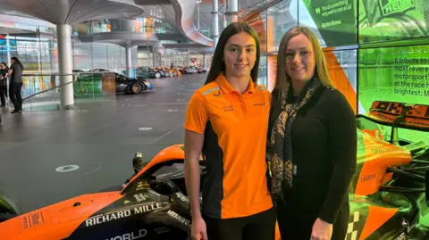 Ella Lloyd and her mother Jessica Lloyd stood together. they are stood in front of the F1 Academy car in the McLauren Technology Centre in Woking, Surrey in November 2024.