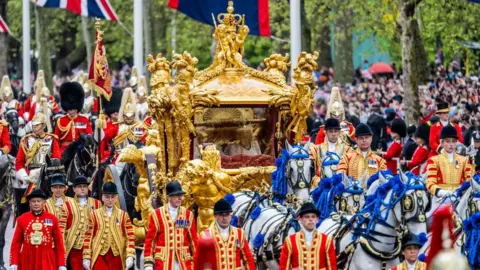 Reuters The King and Queen can be faintly seen within a golden carriage flanked by horses and servicemen and women.