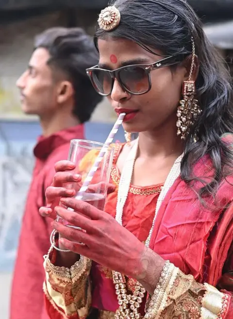 Innovation for Change A girl drinks from a glass with a straw at a fashion show that has gone viral wearing colourful red clothing, jewellery and sunglasses