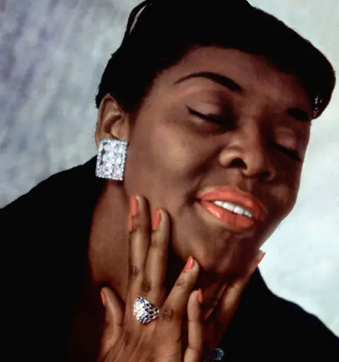 Getty Images Dinah Washington with her hand on her chin and her eyes closed. She is wearing large square diamond earrings and a diamond ring.