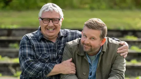 Graeme Hunter / Happy Tramp North  ________________________________________ A bespectacled man with grey hair sits with his arms around the shoulders of a younger bearded man