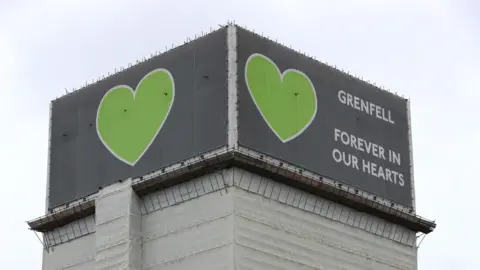 PA Media File photo from 2021 showing a covered Grenfell Tower with grey billboards  at the top featuring green hearts and the message 'Grenfell - forever in our hearts'