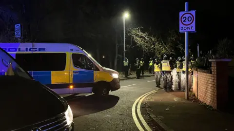 Riot police officers next to a police van on a street in Liberton