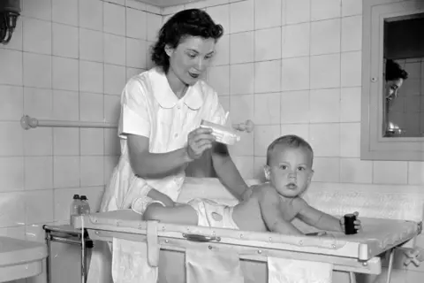 Getty Images Baby being given a bath - a woman putting baby powder on baby - circa 1937-1939.