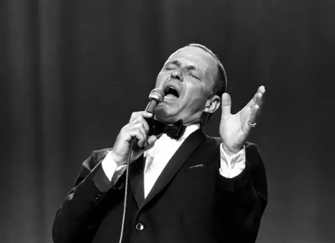 Getty Images Frank Sinatra, wearing a tux, singing into the microphone with his head leaning back