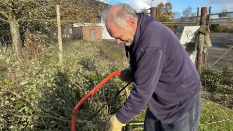 Tony Heath uses a red saw to cut a tree.