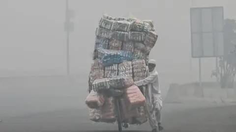 Getty Images A vendor transports food items on his bicycle cart along a road engulfed in smog in Lahore 