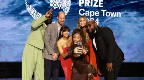 PA Winnie Harlow takes a selfie with the Prince of Wales and other performers and presenters during the Earthshot Prize Awards.