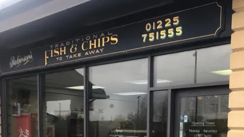 Philip Robinson Front of fish and chip shop with sign that reads "Robinson's Traditional Fish and Chips to take away" and their phone number