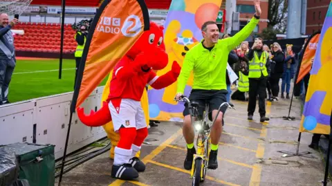 A picture of comedian Paddy McGuinness on a bike with a Pudsey Bear