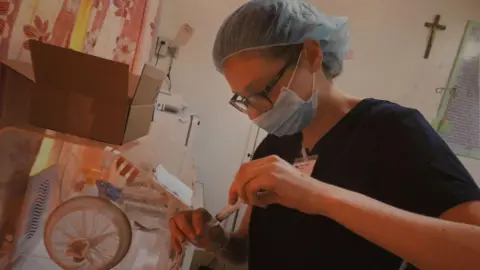 Family photo Mared Foulkes inside a hospital in the Philippines wearing medical scrubs and a face mask, carrying out pharmacy work