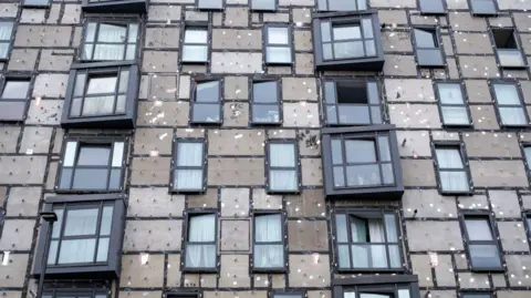 Getty Images Image showing an apartment building which had its cladding removed in 2018 but was waiting for it to be replaced in July 2024. Brown boards and the internal struts and clips for the cladding are visible next to the black windows of the building