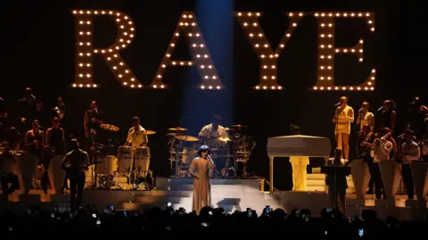 PA Media Raye performing on stage with illuminated letters spelling out Raye behind her