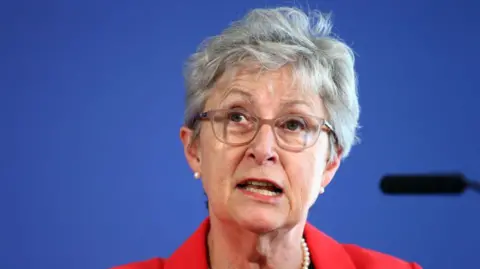 Getty Images Gisela Stuart giving a speech in a red suit in front of a blue background