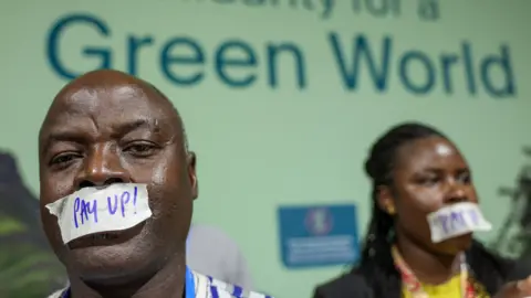 Reuters Two people wear tape over their mouths that reads "Pay up" in front of a sign that reads "Solidarity for a Green World" at COP29 in Baku, Azerbaijan