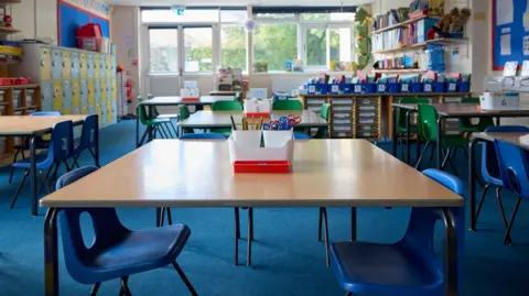 Getty Images Tables and chairs arranged in a primary school classroom. At the back of the room is a window. There are no pupils or teachers present.