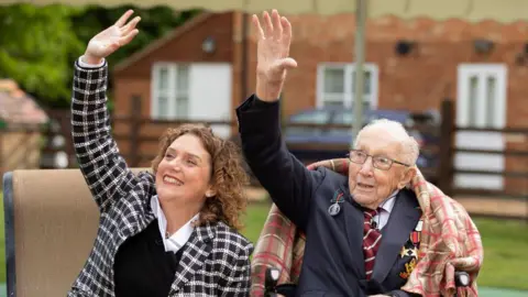 Getty Images Hannah Ingram-Moore and Captain Sir Tom Moore wave at an RAF flypast in a garden