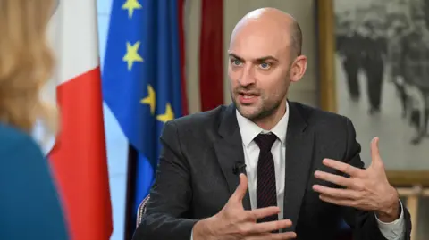 Jeff Overs / BBC French Foreign Minister Jean-Noël Barrot speaking with the BBC's Laura Kuenssberg. He is wearing a dark grey suit, white shirt and dark red striped tie