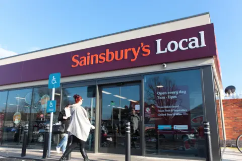 Alamy A woman walking into a Sainsbury's Local convenience store