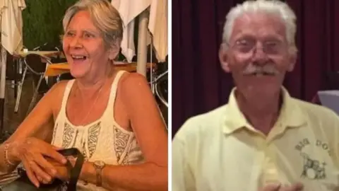 Family Terry is wearing a white vest top and smiling with a bag on her lap. She has short, grey hair, or her hair is possibly tied back. Don is wearing glasses and has a moustache and is wearing a yellow T-shirt.