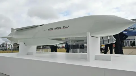 Getty Images A Storm Shadow cruise missile, which is several metres long and has a white glossy outer layer, as well as a "Storm Shadow/SCALP" logo, pictured on a display stand at an air show in Farnborough 