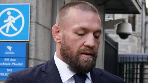 Brian Lawless/PA Wire Conor McGregor outside the High Court in Dublin.  He has a beard, shaved hair and is wearing a navy suit and a white shirt.